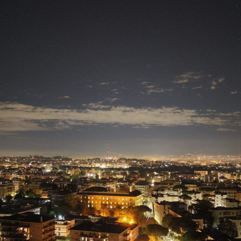 Vista notturna della città con luci brillanti e nuvole sparse nel cielo.